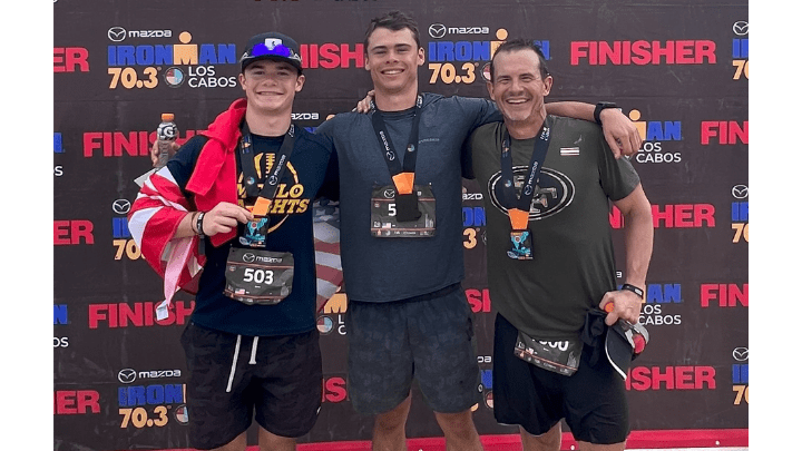 three men in front of ironman banner after finishing