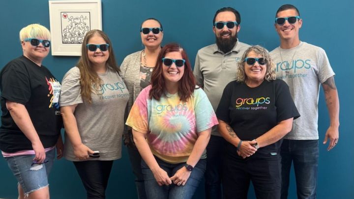 Posed group photo of seven people in sunglasses in an office