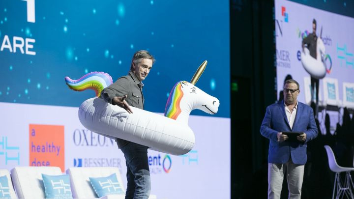 Man on a conference stage wearing a unicorn pool floatie