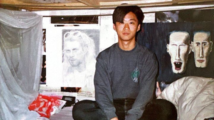 Young man sitting on dorm bed in front of art