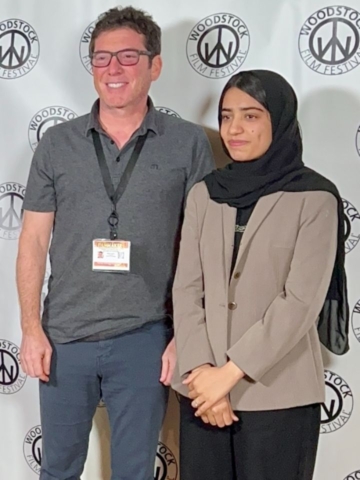 Man and woman standing in front of step and repeat at woodstock film festival