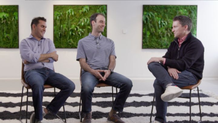 three men sitting on stools talking to each other on panel