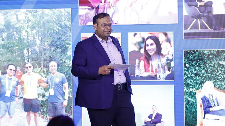 man speaking on stage with photos in background